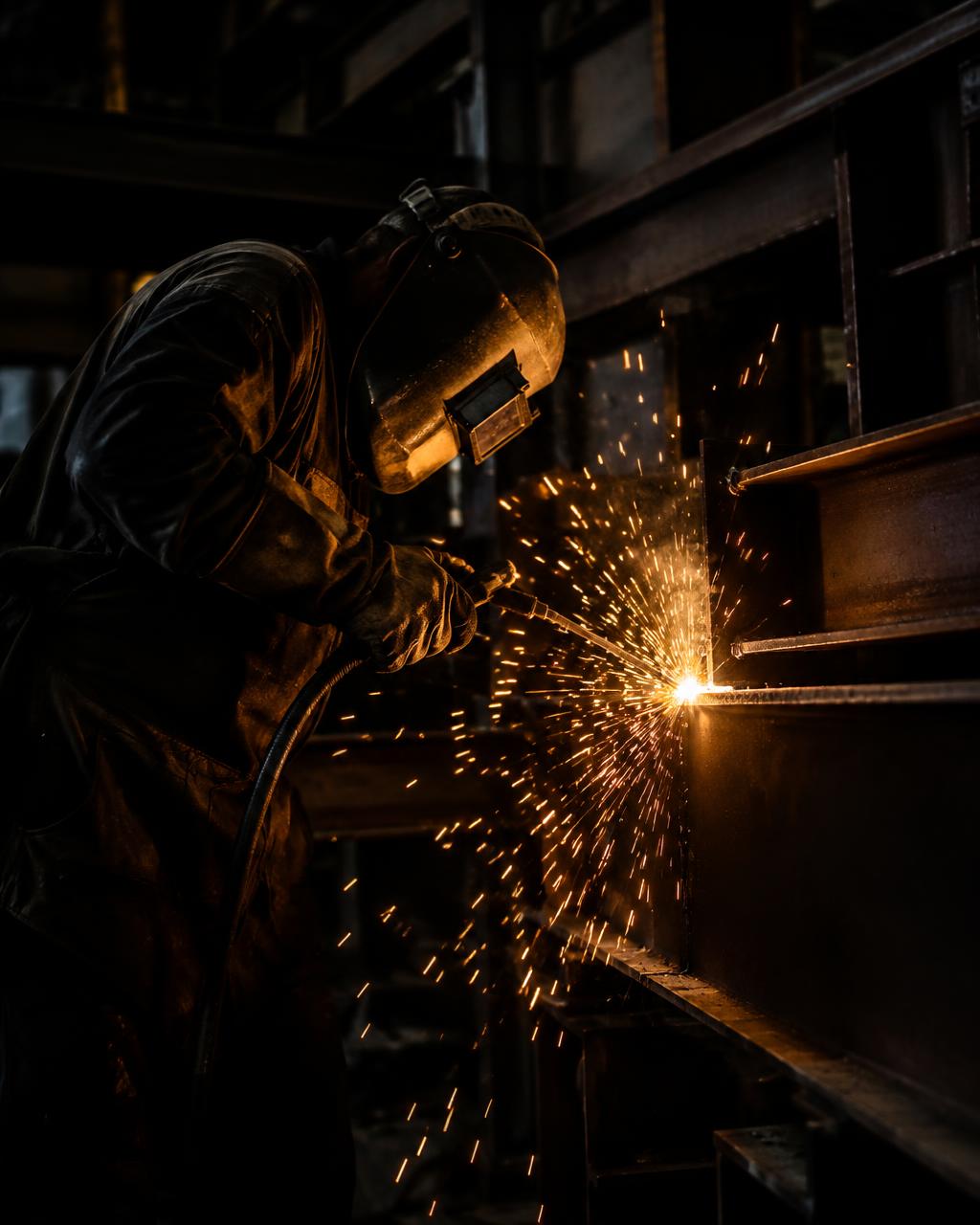 Welder striking an arc in a dark steel workshop